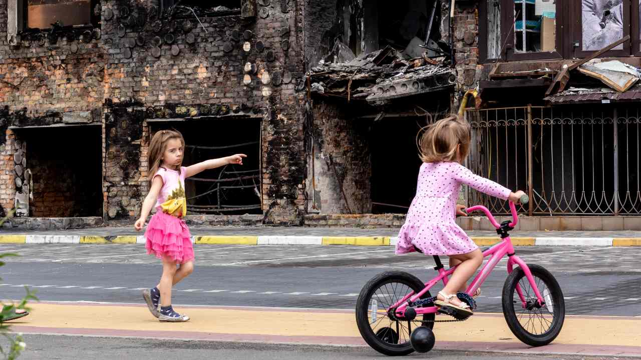 Photo: Two girls are seen in front a residential area affected by bombardment - June 14, 2022 in Bucha, Ukraine. As the Russian Federation invaded Ukraine more than 3 and a half months ago, fierce fighting continues in the East of the country. Some of the most devastated towns since the beginning of the conflict - Irpin and Bucha - build their way to normality. More and more civilians get back to their homes and reestablish their lives. Credit: Photo by Dominika Zarzycka/NurPhoto