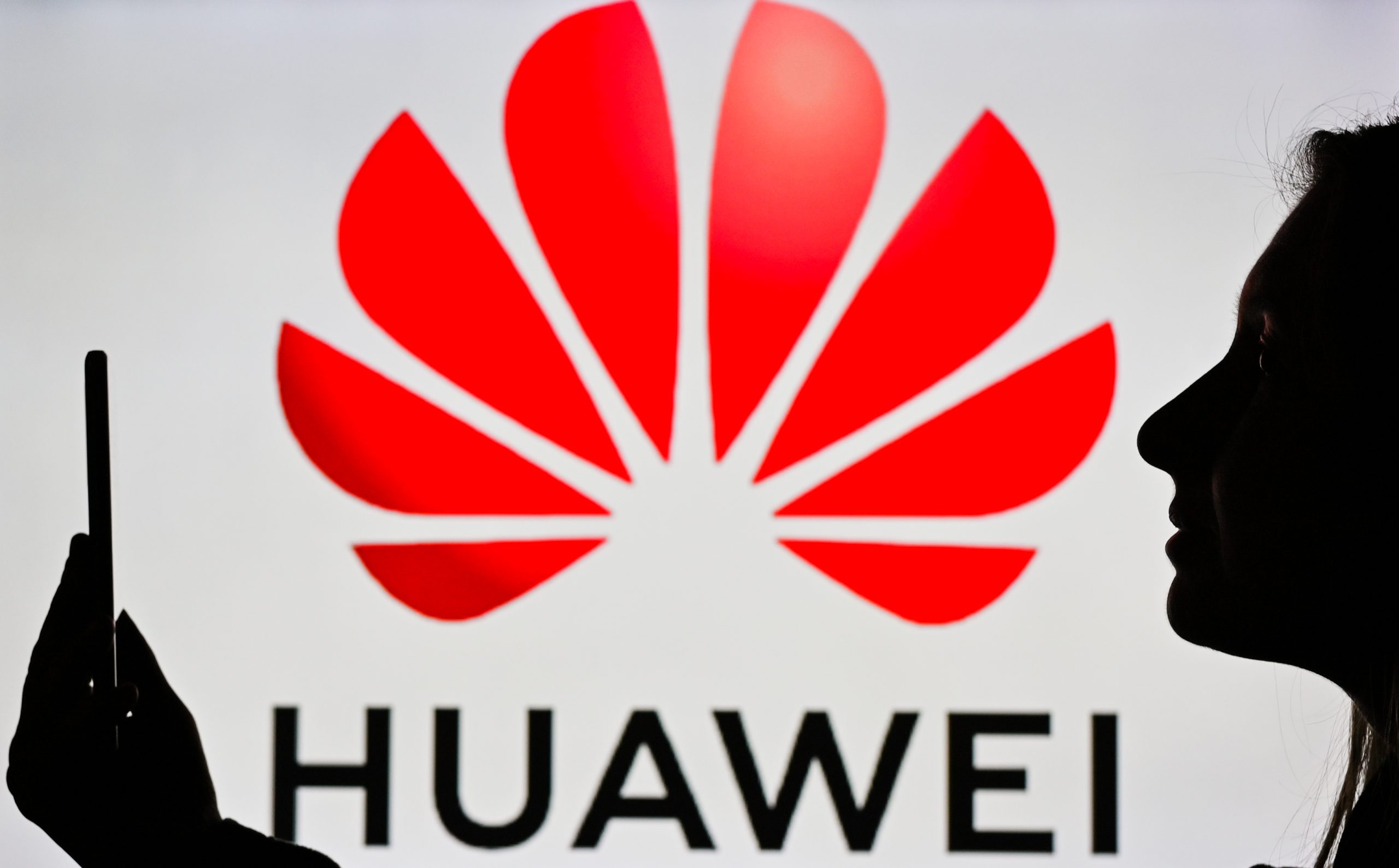 An image of a woman holding a cell phone in front of a Huawei logo displayed on a computer screen. Credit: Artur Widak/NurPhoto