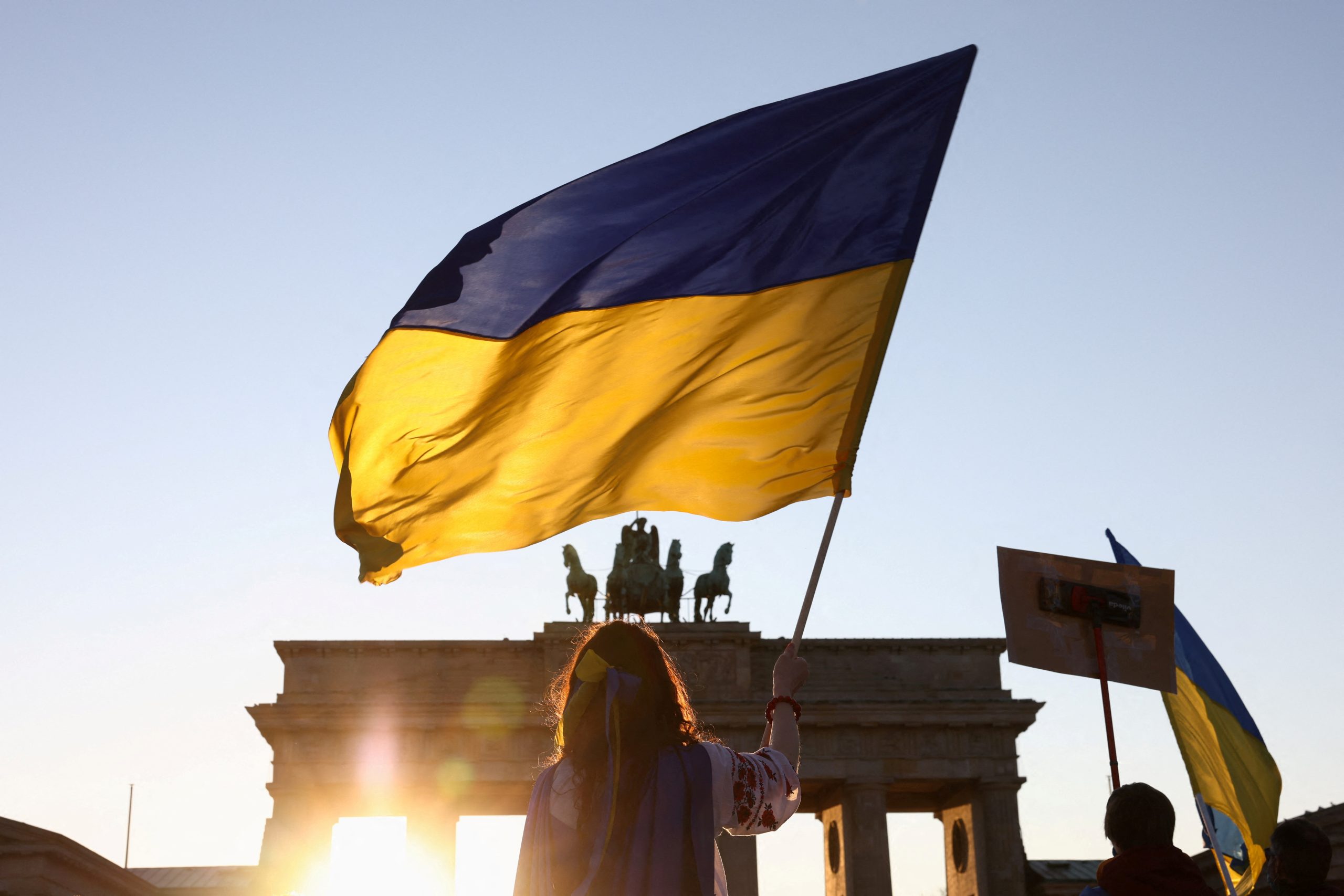 Photo: A person holds a Ukrainian flag during an anti-war demonstration "Stop the War. Peace and Solidarity for the People in Ukraine" against Russia's invasion of Ukraine, next to the Brandenburg Gate in Berlin, Germany, March 13, 2022. Credit: REUTERS/Christian Mang