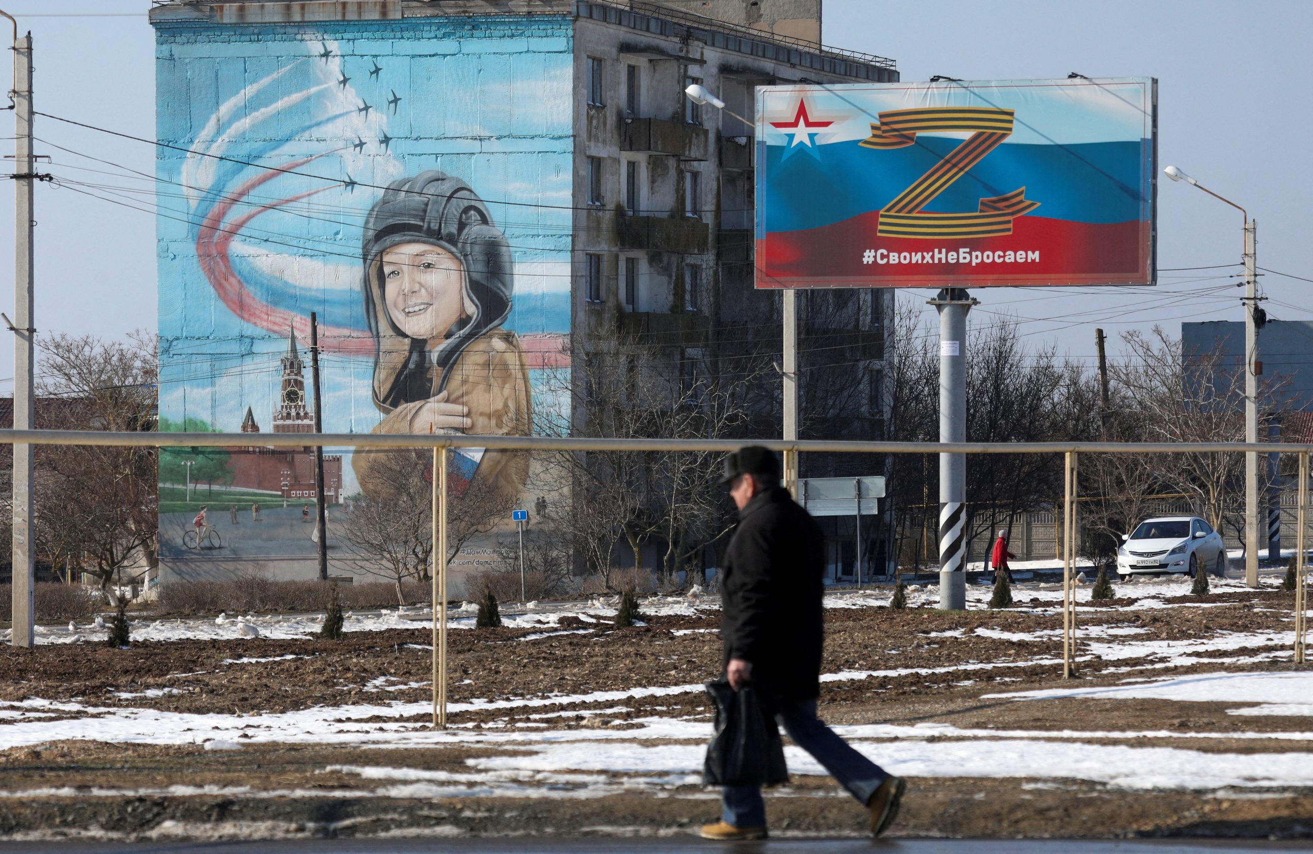 Photo: A pedestrian walks near a board, which displays the symbol "Z" in support of the Russian armed forces involved in the country's military campaign in Ukraine, in the settlement of Chernomorskoye, Crimea, February 11, 2023. A sign on the board reads: "We don't abandon our people". Credit: REUTERS/Alexey Pavlishak